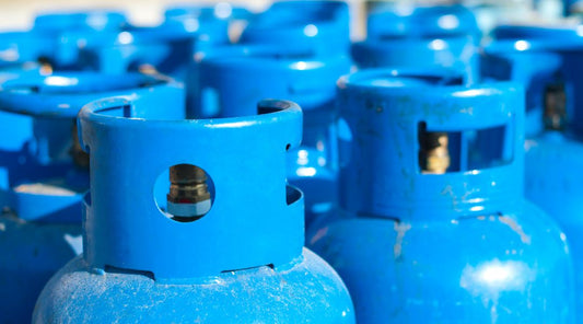 Close-up of multiple blue LPG gas cylinders stored upright in a well-ventilated outdoor area.